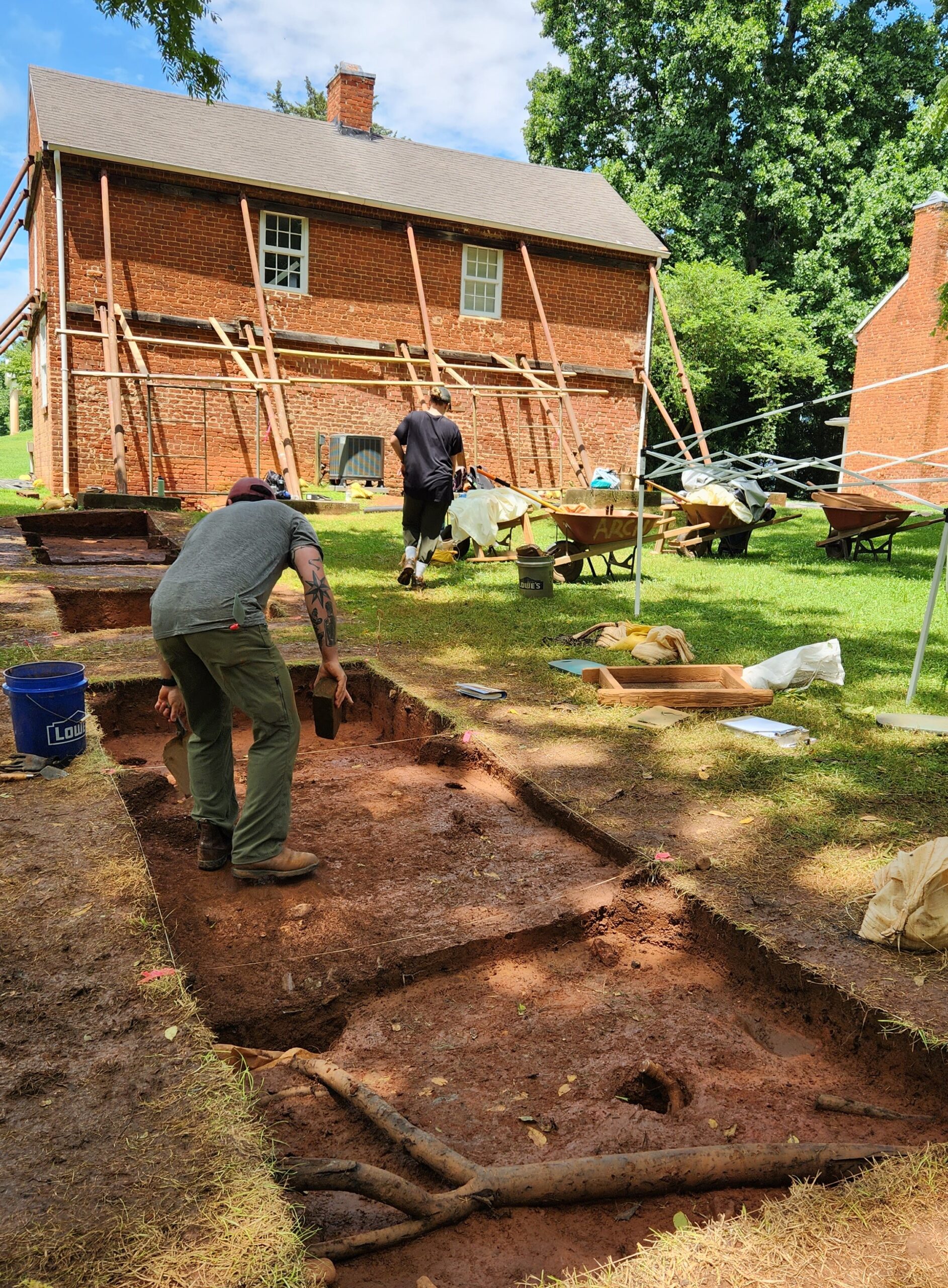 Archaeologists excavating unites behind a brick building.